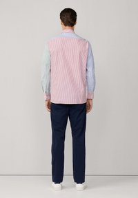 Camisa multicolor con rayas rosas y azules, con mangas largas y cuello. Combinada con pantalones azul marino oscuros y zapatos blancos.
