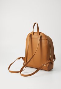 Zaino in pelle tan con un design strutturato, due spallacci regolabili e una tasca frontale con zip. Finitura testurizzata notevole e hardware in tonalità dorata.