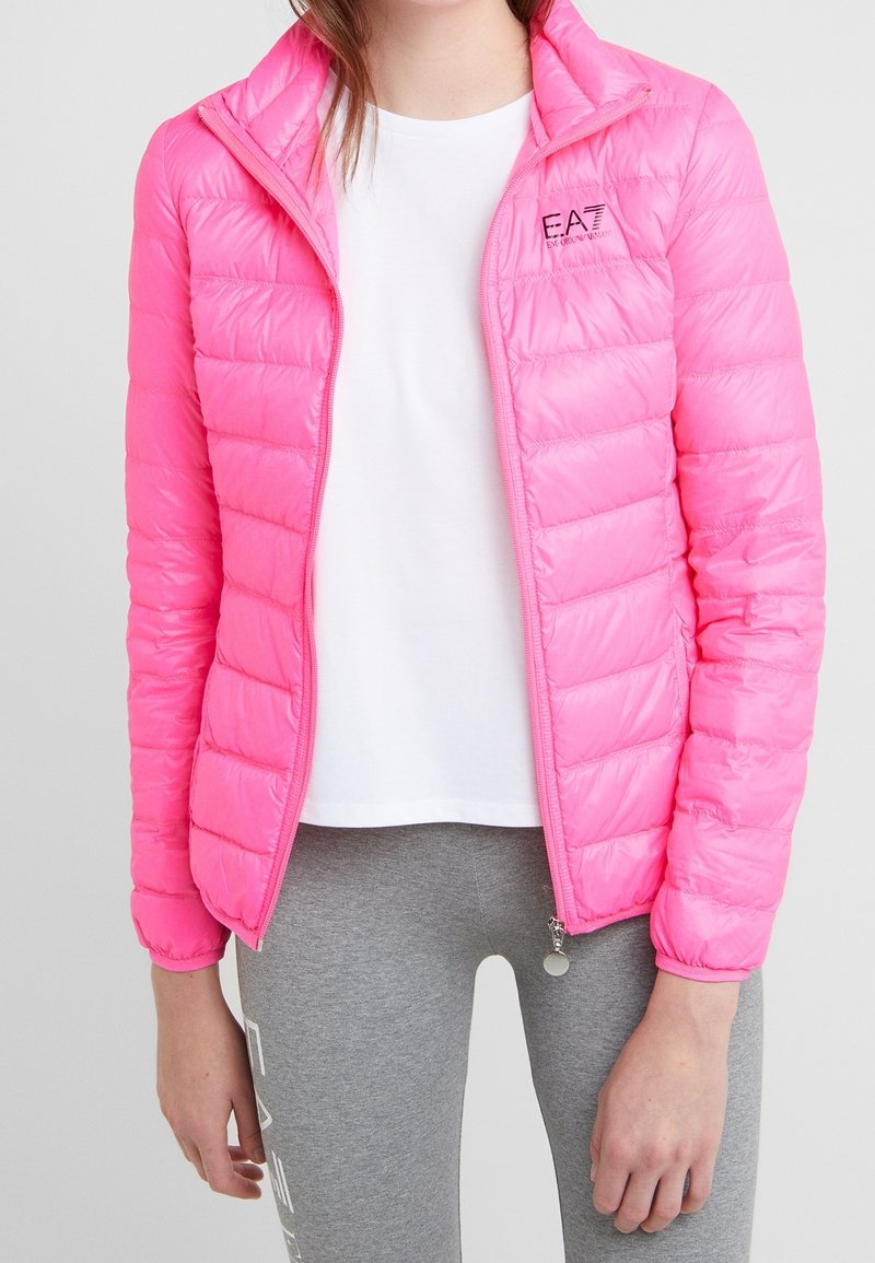 Rosa puffjacka med quiltat mönster, full dragkedja och hög krage. Har en liten logotyp på vänster bröst och matchande dragkedjeinslag.