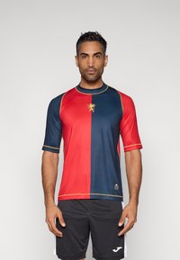 Koszulka sportowa z krótkim rękawem z czerwono-niebieskim podziałem, złotymi akcentami i emblematem lwa na klatce piersiowej. Wykonana z gładkiego, rozciągliwego materiału.