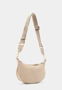 Borsa a tracolla in pelle beige con forma curvata, hardware dorato e una tracolla regolabile texturizzata. Presenta una chiusura con zip e dettagli con logo.