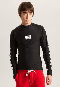 Rash guard noir à manches longues avec le logo Vans sur la poitrine et un motif damier blanc sur la manche gauche ; tissu lisse et extensible.