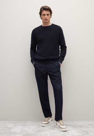 Navy sweater with textured knit, paired with fitted navy trousers and cream sneakers with gold accents. Simple design, casual look.