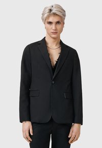 Svart blazer med en knapp, två framfickor och en skräddarsydd passform. Slät tyg med matt yta. Modell bär en djupurringad skjorta under.