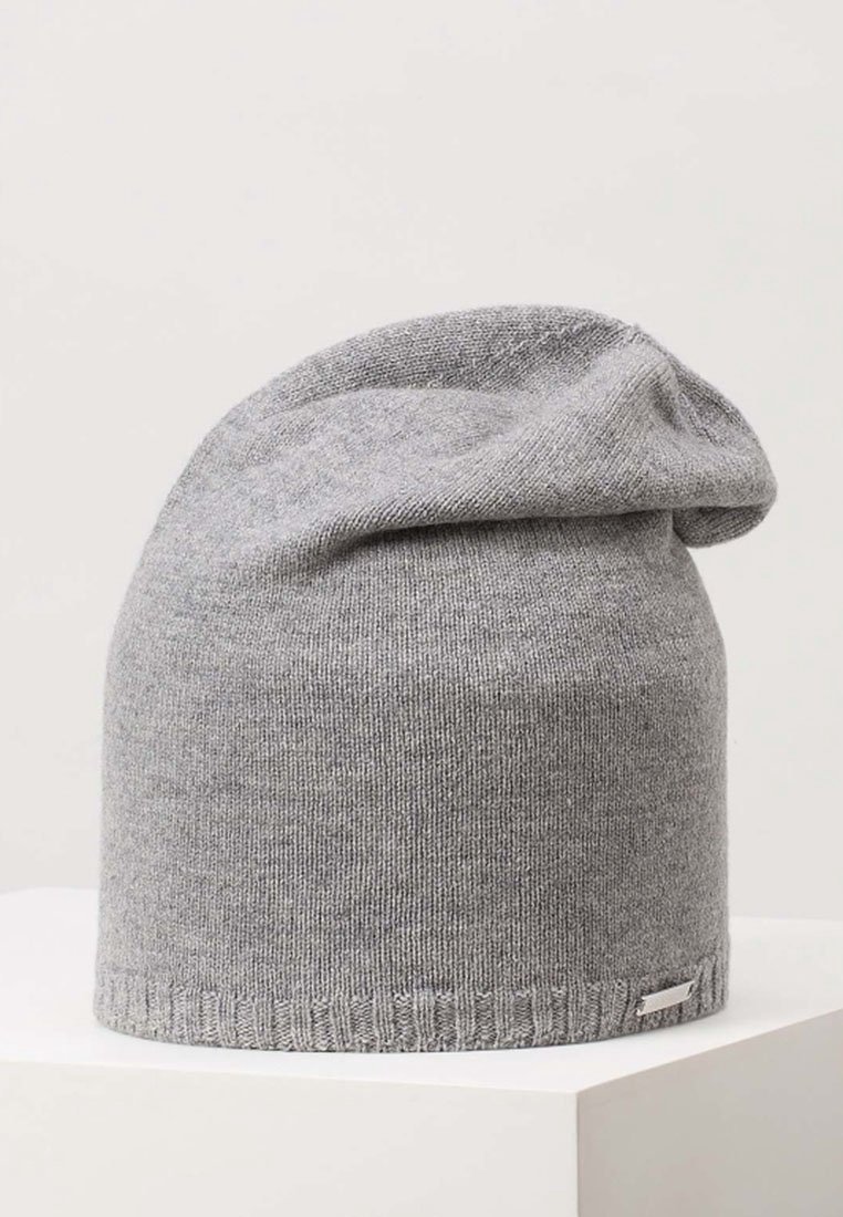 Bonnet en tricot gris doux avec une partie supérieure repliée et une petite étiquette métallique rectangulaire près de l'ourlet côtelé, présenté sur un socle blanc.