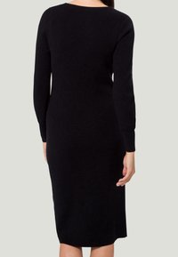 Robe noire en maille côtelée avec de longues manches, un col rond et une silhouette ajustée, atteignant le milieu du mollet.