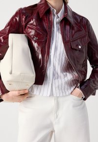 Bordowa kurtka ze skóry lakierowanej z ostrym kołnierzem, z dwoma kieszeniami na piersi. W połączeniu z białą koszulą w prążki i białymi spodniami.