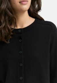 Zwarte cardigan met ronde halslijn en ribgebreid trim. Heeft zes zwarte knopen aan de voorkant, gemaakt van een zachte textuur.