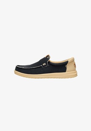 Zapato casual para hombre tipo slip-on con empeine de tela azul marino, talón y cuello beige, y suela color cuero con detalles cosidos.