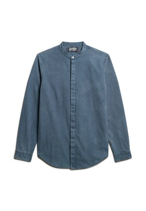 Camisa de denim en azul medio, con cuello mao, mangas largas, cierre frontal de botones y dobladillo redondeado. Tejido texturizado con sutiles detalles de patrón.