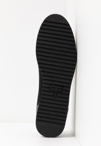 Suela de zapato de goma negra con ranuras horizontales para tracción, que presenta una marca en relieve y una puntera suave y redondeada.