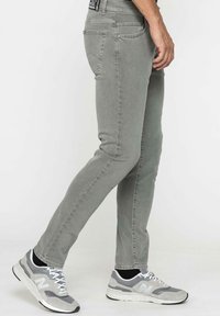 Jeans en denim extensible gris avec une coupe slim. Comprend cinq poches, des passants de ceinture et une texture subtile. Associés à des chaussures de sport gris et blanc.