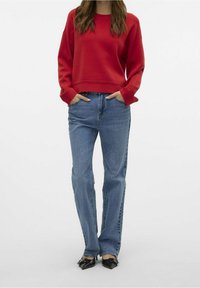 Sweat-shirt court rouge à manches longues, associé à un jean droit bleu et des chaussures noires à bout pointu. Tissu lisse et coupe décontractée.