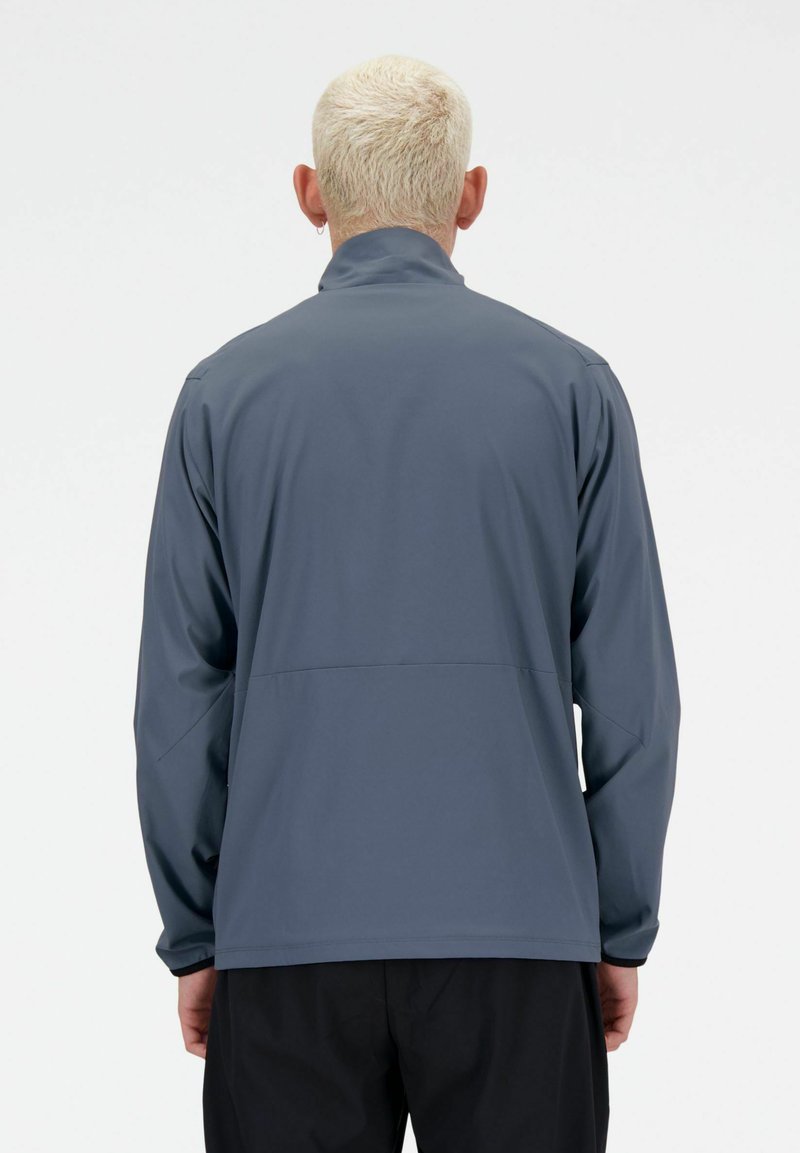 Chaqueta ligera gris con cuello alto y mangas largas, que presenta una textura suave y una costura en la parte de atrás como detalle de diseño.