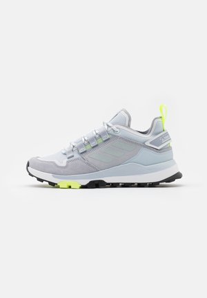 Lysegrå og hvide Adidas Terrex sneakers med sort sål og neon gul træksnor og detaljer, vist fra siden på en hvid baggrund.