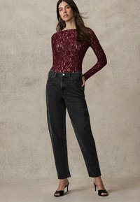Bodysuit en dentelle bordeaux associé à un jean noir taille haute. La tenue comprend des manches longues et une coupe décontractée, complétée par des talons noirs.