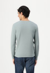 Lichtblauwe geribbelde trui met lange mouwen en een ronde halslijn, gecombineerd met donkere denim jeans met achterzakken en stikdetails.