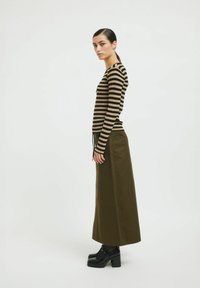 Suéter de rayas de manga larga con canalé en negro y beige, combinado con una falda verde oliva de cintura alta y zapatos negros de tacón grueso.
