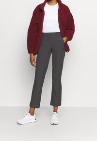 Bordeaux fleece jack, wit t-shirt, grijze broek met een rechte pijp, en witte sportschoenen. Heeft een gestructureerde afwerking en subtiele branding.