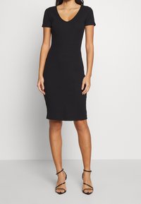 Schwarzes, geripptes Midikleid mit kurzen Ärmeln und V-Ausschnitt. Die taillierte Passform betont die Taille und endet knapp unter dem Knie. Glatte Textur.