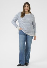 Pull en tricot rayé bleu clair et blanc avec des poignets unis de couleur claire, associé à un jean en denim bleu évasé. Coupe décontractée avec poches latérales.