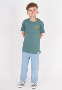 Grünes Baumwoll-T-Shirt mit "BOFR 2017" in Orange bedruckt, kombiniert mit hellblauen Jeans im Straight-Leg-Stil und grünen Sneakers.