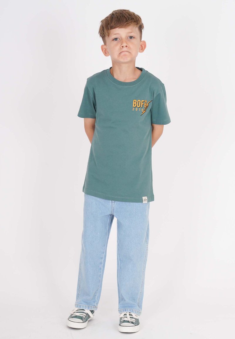 Grünes Baumwoll-T-Shirt mit "BOFR 2017" in Orange bedruckt, kombiniert mit hellblauen Jeans im Straight-Leg-Stil und grünen Sneakers.