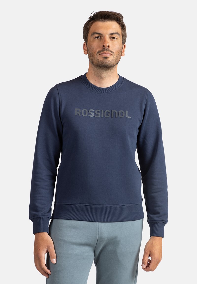 Sudadera azul marino con cuello redondo, puños y cintura acanalados. Presenta un logo "ROSSIGNOL" en negro mate en el pecho. Textura suave.