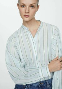 Lichte, gestreepte blouse in lichtgroen en wit. Voorzien van een knoopsluiting aan de voorkant en een bandkraag met licht opgezette mouwen.