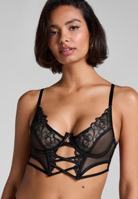 Zwarte lingerie met doorschijnende meshstof, bloemenborduurwerk en een gestructureerd ontwerp. Voorzien van decoratieve hardware en kruislingse details.