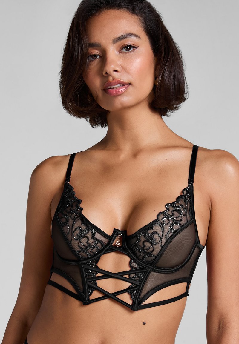 Zwarte lingerie met doorschijnende meshstof, bloemenborduurwerk en een gestructureerd ontwerp. Voorzien van decoratieve hardware en kruislingse details.