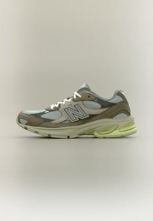 Lys grå og beige sportssko med mesh-paneler, hvite lisser og polstret såle med neon gule aksenter, sidevisning.