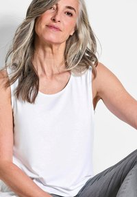 Witte mouwloze top van zacht stof met een ronde halslijn, gecombineerd met grijze broeken. Recht gesneden, minimalistisch ontwerp.