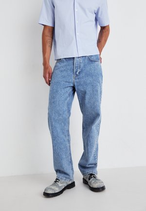 Lysblå denim jeans med løs pasform, der har et klassisk fem-lomme design og kontraststing, parret med grå teksturerede sko.