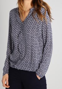 Blusa a fantasia navy con scollo a V, maniche lunghe e vestibilità morbida; presenta un tessuto testa di morbido con un delicato design astratto.
