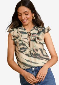Blusa senza maniche con scollatura a volant, realizzata in tessuto beige con strisce verdi e rosa. L'apertura legata sul davanti aggiunge un tocco di dettaglio.