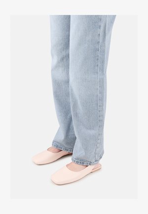 Scarpe slip-on aperte sul retro di colore rosa chiaro con una punta quadrata. Indossate con jeans dritti di un leggero blu sbiadito. Texture liscia.