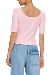 Różowa bluzka z krótkim rękawem o szerokim dekolcie z tyłu, wykonana z miękkiego materiału, w połączeniu z jasnoniebieskimi dżinsami z dużą kieszenią.