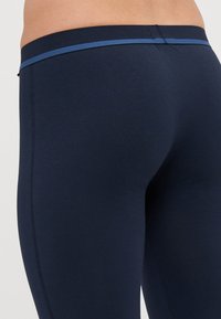 Marina leggings med en slät textur, som har en kontrasterande blå midja. Designen är åtsittande och betonar en strömlinjeformad siluett.