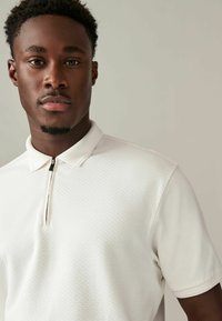 Witte polo shirt met een gestructureerd patroon, voorzien van een halve rits en een kraag. Korte mouwen en een schone, eenvoudige uitstraling.
