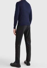 Pull ajusté bleu marine à manches longues associé à un pantalon noir droit. Chaussures élégantes noires avec une texture lisse.