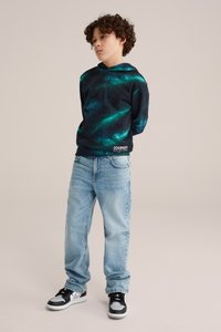Felpa nera con motivo spaziale verde e blu, tasca a marsupio frontale, abbinata a jeans in denim blu chiaro e sneakers nere.