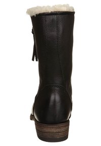 Botín de cuero negro con un puño de peluche blanco, superficie texturizada y un tacón de madera apilada. Incluye un detalle con cremallera lateral.