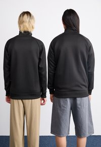 Sorte sweatshirts med høje kraver, ribbede manchetter, parret med beige vide bukser og grå shorts. Glat tekstur, afslappet pasform.