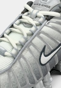 Zbliżenie szarego trampka Nike Shox z białymi sznurowadłami i widoczną wyprofilowaną podeszwą.