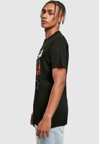 Sort bomulds T-shirt med et farverigt grafisk design på fronten. Korte ærmer og en klassisk pasform. Lyseblå jeans bæres til.