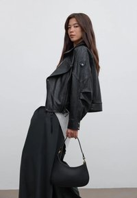 Zwarte leren cropped jack met oversized revers en knoopdetails, gecombineerd met een zwarte rok en een kleine zwarte handtas.