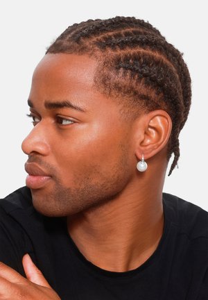 Orecchino di perle con hardware in argento, indossato da un modello con capelli intrecciati, su uno sfondo neutro. Camicia nera visibile.