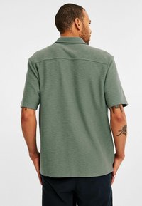 Korte mouw shirt in een gedempte groene stof met een textuurafwerking, voorzien van een klassieke kraag en een rechte zoom. Zichtbare schoudernaad details.