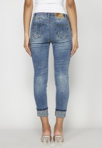 Slim jeans i ljusblå denim med en urtvättad finish. Har dekorativa bakfickor med utsmyckningar och uppvikta fållar med mönstrad kant.